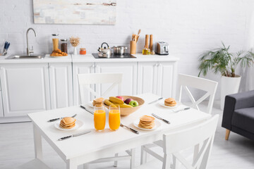fresh orange juice, tasty pancakes and fruits on table in modern kitchen
