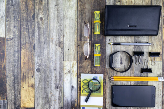 Office financial flat lay still life with 200 euro bills, magnifying glass, purse, smartphone and stationery over a grey wood background with copyspace