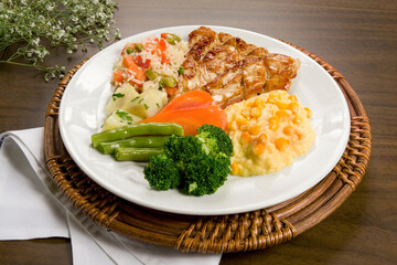 Filé de frango grelhado com salada de maionese, creme de milho verde e legumes, sobre tampo de madeira.