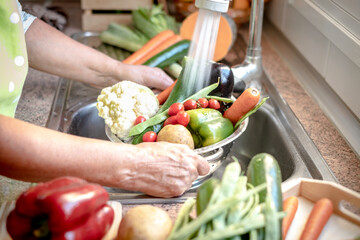 Woman's hands holding a basket of vegetables under running water to wash them