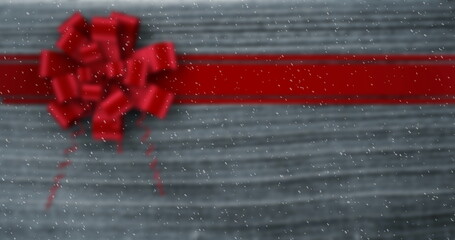 Image of snow falling against christmas present ribbon on wood