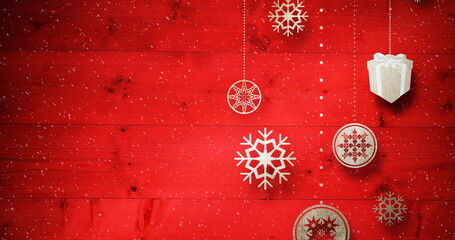 Image of snow falling against christmas decoration on red boards