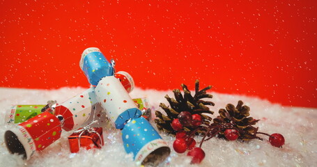 Image of snow falling against christmas crackers decorations on red