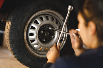 Mixed race female car mechanic wearing overalls, unbolting wheel of car