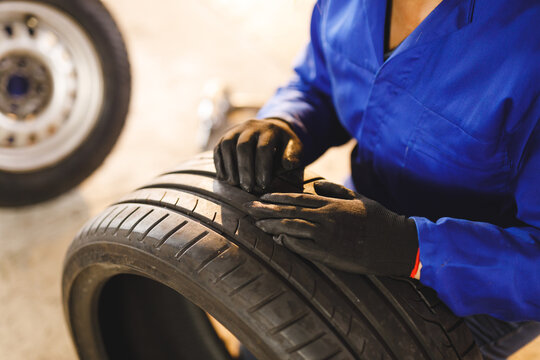 Midsection of mixed race female car mechanic wearing overalls, checking tire - Powered by Adobe