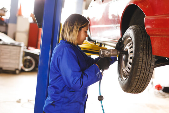 Mixed race female car mechanic wearing overalls, unbolting wheel of car