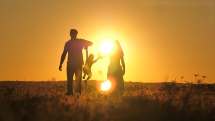 A small child walks with mom and dad at a bright sunset in the sky. Meet the sunrise with your...