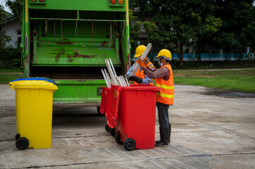 Garbage men working together on emptying dustbins for trash removal with truck loading waste and trash bin.