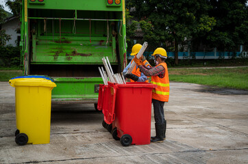 Garbage men working together on emptying dustbins for trash removal with truck loading waste and...