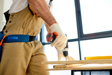 Close-up hands of Handyman screwing wood using drill, Diy at Home concept. Woodworking, man in gloves making a hole in wooden board. focus on hands