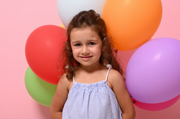 Fototapeta na wymiar Isolated portrait, head shot, close-up of beautiful cheerful 4 years baby girl with multicolored balloons smiling looking at camera. Pink background copy space