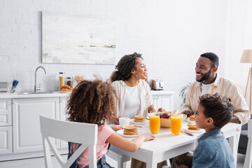 african american couple smiling during breakfast with children in kitchen