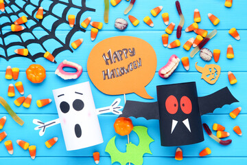 Text Happy Halloween with candies, paper ghosts, pumpkin and spiderweb on blue wooden background
