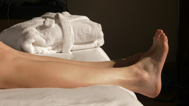 Close-up camera shot of young woman naked feets. Female stretch her feets in the morning. Morning sun, white sheet.
