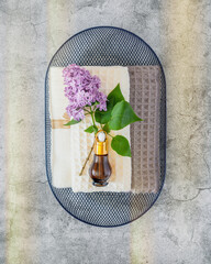 A blue basket filled with folded towels, bottle of serum and lilac flowers on a gray background. Wellness, spa, relax and me time banner. Concept of skinimalism and multiuse care product. Flat lay
