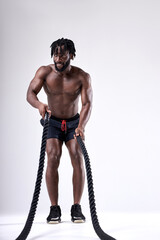 Fototapeta na wymiar Black muscular man working out with heavy ropes. sporty male with naked torso isolated on white background. Strength and motivation. Front view. Full-length portrait.