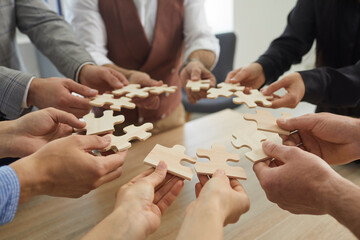 Team of business people joining pieces of jigsaw puzzle, closeup shot of hands holding jigsaw parts...