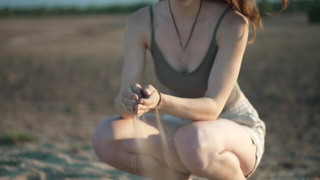 Young woman crouching in desert letting sand slipping through hands
