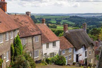 Old English houses with red roof tiles and thatched roofs and with green hills in the background (Golden hill) in the picturesque village of Shaftesbury, Dorset, England.