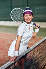Are you ready to play. Happy sexy beautiful woman in sports clothing holding tennis racket and smiling, posing at camera. Fitness lady in short skirt and cap before tennis game, prepared to play