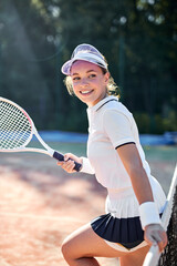 Beautiful female tennis player in white uniform stands next to net posing with racket, attractive caucasian lady in cap looking at side, smiling, feeling happiness after game. People lifestyle, sport