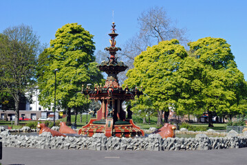Fototapeta na wymiar Ornate Cast Iron Fountain in Public Park with Trees & Blue Sky 