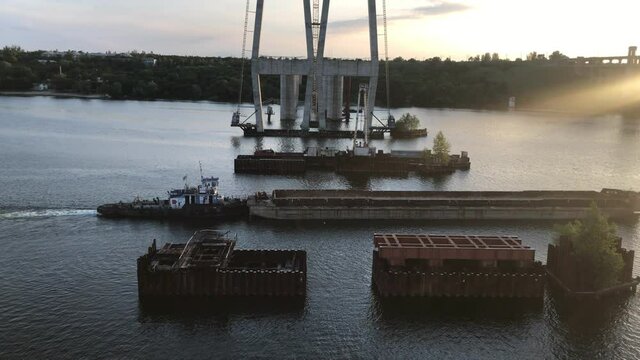a large cargo barge without cargo passes along a wide river near the construction of bridges in the evening at sunset