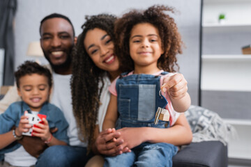 Obraz premium happy african american child holding key near blurred family