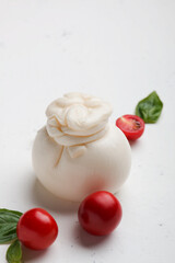 Delicious fresh cheese made from cream and milk - burrata. Italian tender cheese with tomatoes and herbs on a light background