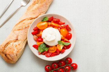 Delicious fresh cheese made from cream and milk - burrata. Italian tender cheese with fork and knife. Bread and salad of tomatoes and herbs, cherry tomatoes on a twig.