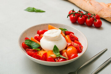Delicious fresh cheese made from cream and milk - burrata. Italian tender cheese with fork and knife. Bread and salad of tomatoes and herbs, cherry tomatoes on a twig.