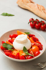 Delicious fresh cheese made from cream and milk - burrata. Italian tender cheese with fork and knife. Bread and salad of tomatoes and herbs, cherry tomatoes on a twig.