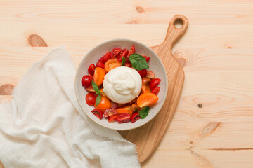 Delicious fresh cheese made from cream and milk - burrata. Italian tender cheese with tomato and greens salad on a light wooden board.