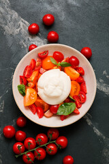 Delicious fresh cheese made from cream and milk - burrata. Italian tender cheese with tomato and greens salad on dark marble background
