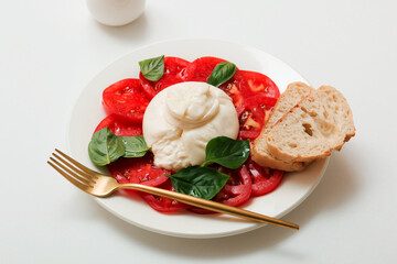 Delicious fresh cheese made from cream and milk - burrata. Italian tender cheese with tomato and greens salad, bread and olive oil.