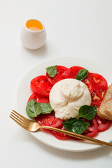 Delicious fresh cheese made from cream and milk - burrata. Italian tender cheese with tomato and greens salad, bread and olive oil.