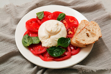 Delicious fresh cheese made from cream and milk - burrata. Italian tender cheese with tomato and greens salad, bread and olive oil.