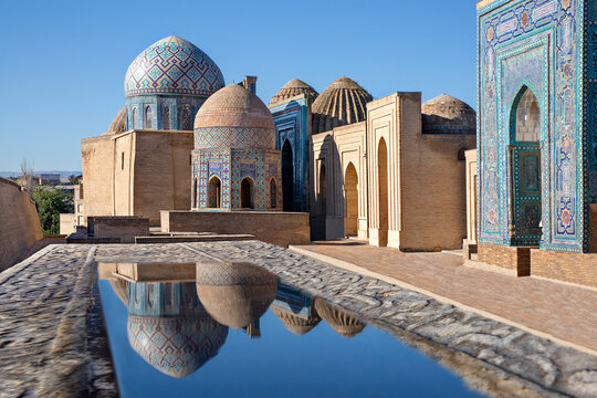 Mausoleums and domes of the historical cemetery of Shahi Zinda and their reflections in puddle, Samarkand, Uzbekistan.