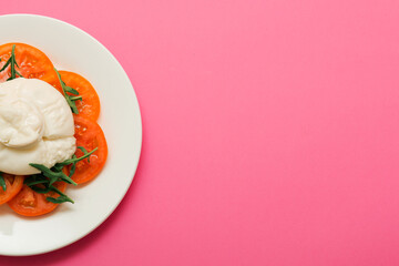 Delicious fresh cheese made from cream and milk - burrata. Italian tender cheese with tomato and greens salad on a bright pink background