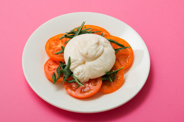 Delicious fresh cheese made from cream and milk - burrata. Italian tender cheese with tomato and greens salad on a bright pink background