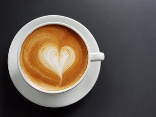 Perfect cup of cappuccino with latte art heart in white cup on black table background.