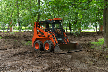 Skid steer loader clearing the site in public park moving soil and performing landscaping works for...
