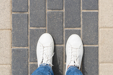 White leather sneakers on paving stones background. Walks through the city streets wearing comfortable footwear.