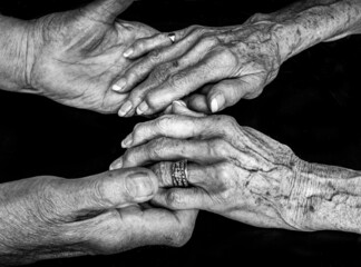 A black and white image of an elderly couple holding hands. The woman is wearing a wedding ring and both appear to have advanced arthritis in their knuckles. The image conveys a feeling of tender love - obrazy, fototapety, plakaty
