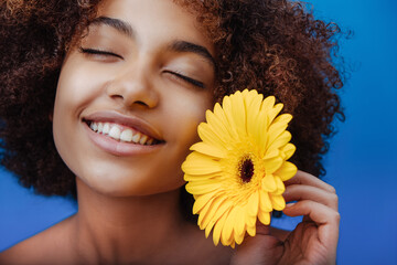 Mixed race young woman with short curly brown hair and bare shoulders holds yellow flower and...
