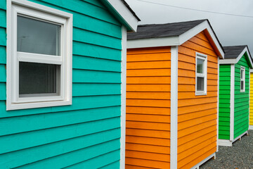 The exterior of bright orange, teal, yellow, and green shed with narrow wooden horizontal clapboard...