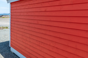 Bright red narrow wooden horizontal clapboard siding on the exterior wall of the building. There's...