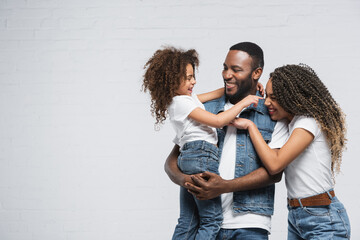 excited african american family looking at each other and hugging on grey