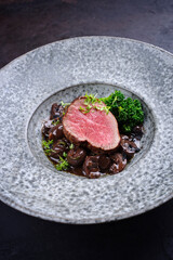 Modern style traditional fried dry aged angus beef filet medaillons natural with mushrooms and baby broccoli in red wine sauce served as close-up on a design plate