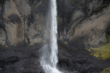 Fototapeta na wymiar dünner hoher Wasserfall vor dunklen Felsen